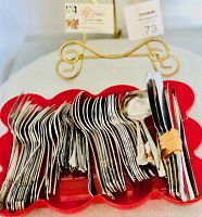 Photo showing a large collection of silver-colored forks, spoons, and knives arranged in a red scalloped dish with a gold decorative stand in the background.
