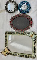 Four decorative photo frames arranged on a surface: oval, round with bead-like designs, blue round, and butterfly decorated rectangular frame.