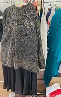 Black long-sleeve top with gold swirling sequin pattern draped over black skirt or bottom, hanging on a rack with other garments.