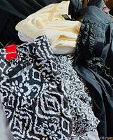 Photo showing mixed women's tops including black and white patterned blouse, cream blouse with embroidery, and black ruffled sleeveless top.