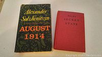 Two books side by side on a flat surface, showing front covers: "August 1914" with a black patterned jacket and "Story of a Secret State" with red cover.