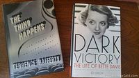 Front covers of two hardcover books: "The Thing Happens" by Terrence Rafferty and "Dark Victory: The Life of Bette Davis" by Ed Sikov, laid side by side on a wooden surface.