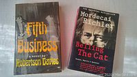 Fifth Business hardcover with dust jacket and Belling The Cat paperback cover photo side by side