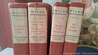 Four red-bound volumes of Oscar Wilde's works arranged upright showing spine titles and volume numbers.