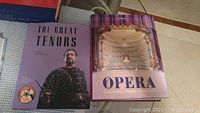 Two opera books side by side on a checkered surface. One titled 'The Great Tenors' and the other 'Opera: Composers Works Performers' shows the cover images clearly.