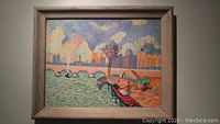 Framed oil painting depicting impressionist riverside cityscape with bridge, boats, and buildings.