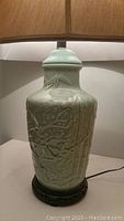 Close-up of the jade green ceramic lamp body showing embossed floral and bamboo patterns and round carved wood base.