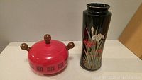 Front view of red enameled metal pot with wood handles and ceramic floral vase