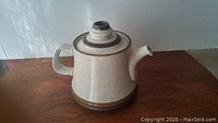 Side view of large Denby tea pot showing handle, spout, and lid with brown band accents on speckled beige ceramic.