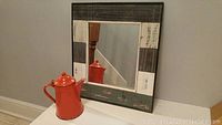 Photo of rustic multicolor wooden framed mirror with enameled metal coffee pot in front.