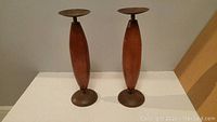 Pair of 15 inch tall wooden sculptures with metal circular tops and bases on a flat surface.