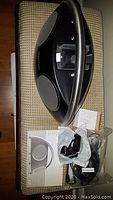 Top view of the black Harman Kardon speaker showing the iPod/iPhone dock, two speakers, remote control, AC adapter, and user manuals on a bench.