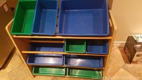 Front view of the toy organizer showing 4 tiers and 9 plastic bins in blue and green.