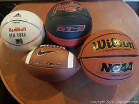 Photo showing a set of four inflated sports balls including Adidas soccer ball, Wilson basketball, Rawlings outdoor basketball, and Nike football on a round table surface.