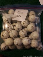 Clear photo of approximately 40 white golf range balls in a clear plastic resealable bag. Balls show black alignment lines and numbers, mostly Wilson brand.