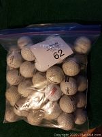 Clear plastic resealable bag containing approximately 40 used golf balls with some branding visible, showing wear and dirt marks from prior use on golf range.