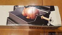 Box showing the rotisserie set with a chicken mounted and grilling, showcasing the rods and wooden handle.
