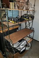 Front view of the shelving unit showing the five wicker shelves and metal frame with decorative scrollwork and items placed on shelves.