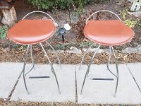 Front view of two butterscotch leather and metal bar stools showing seat shape and metal legs.