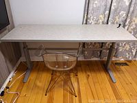 Front view of full desk showing laminate top, steel base and transparent chair.