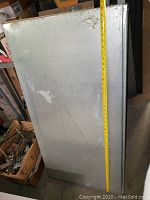 Metal shelf panel vertically positioned with measuring tape showing length close to 48 inches (4 ft)