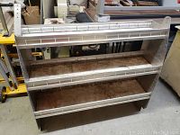 Front-on photo of the metal shelving unit showing three shelves and side panels with adjustment holes.