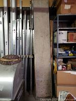 Photo showing the full length of the plywood decked scaffolding platform standing vertically among other stored metal items.