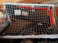 Mini hockey goal showing white PVC pipe frame and white sleeve netting attached to a top shelf red frame.