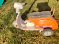 Side view showing orange plastic body, white front panel, two rear wheels and overall condition.