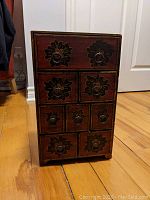 Full front view of the wooden decorative box showcasing all nine drawers with floral design and metal ring handles.