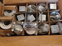 Box containing 12 recessed lighting housings and trims organized in individual compartments for protection.