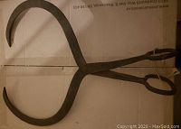 Top view of vintage cast iron hook/tong showing entire tool and its curved arms.