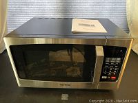Front view of Toshiba EM925A5A-SS microwave oven with stainless steel finish and control panel visible, original manual on top.
