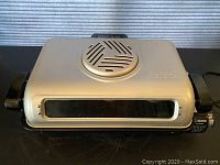 Closed view of metallic gray fish roaster with control knob and viewing window on front.