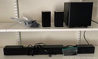Sound bar, wireless subwoofer, two rear satellite speakers, and cables arranged on shelves.