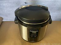 Full view of Cuisinart pressure cooker showing brushed stainless steel body and closed black lid with handle.