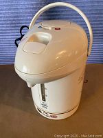 Full view of the white Zojirushi electric water boiler with handle and push button dispensing system on table.