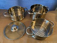 Complete Fagor stainless steel 2-quart double boiler set including base pot, steamer insert, and glass lid all displayed with large riveted loop handles on each piece.