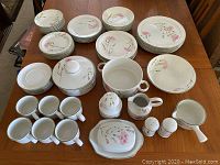 Full set displayed on table showing arrangement of plates, bowls, cups and serving pieces with floral pattern