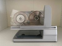 Side view of the Chef's Choice 610 electric food slicer showing two different blades in packaging on the slicer platform.