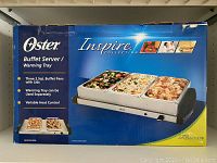 Box of Oster Inspire buffet server showing branding and product features including three 2.5 quart buffet pans with lids, warming tray can be used separately and variable heat control.