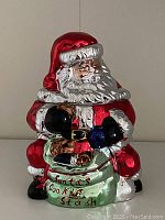 Front view of a shiny ceramic cookie jar in the shape of Santa Claus holding a green container labeled 'Santa's Cookie Stash'.