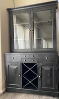 Full view of the black wood wine cabinet with hutch, showing the lower cabinet with drawers, cupboards, wine bottle storage, and the upper hutch with glass doors.