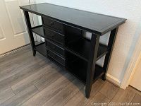 Side view of black wooden side table showing four drawers in the center and open shelves on both sides, overall view of the item.