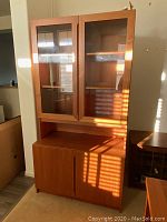Front view of the cabinet and illuminated hutch showing the teak wood frame, glass doors on the hutch, and two solid doors on the bottom cabinet.
