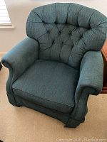 Front view showing button-tufted back and cushioned arms with pleated design and kick-pleat skirt.