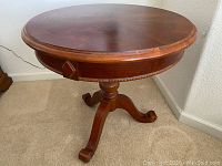 Full view of circular side table showing carved pedestal base and curved legs with scroll feet.