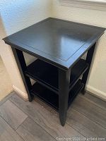 Front left angle view of the black corner table showing the top surface and leg detail.