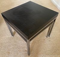 Close-up of larger table showing square black wood-grain finish top and stainless steel legs