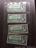 Four uncirculated Canadian one dollar bills in protective sleeves, showing front with Queen Elizabeth II portrait.